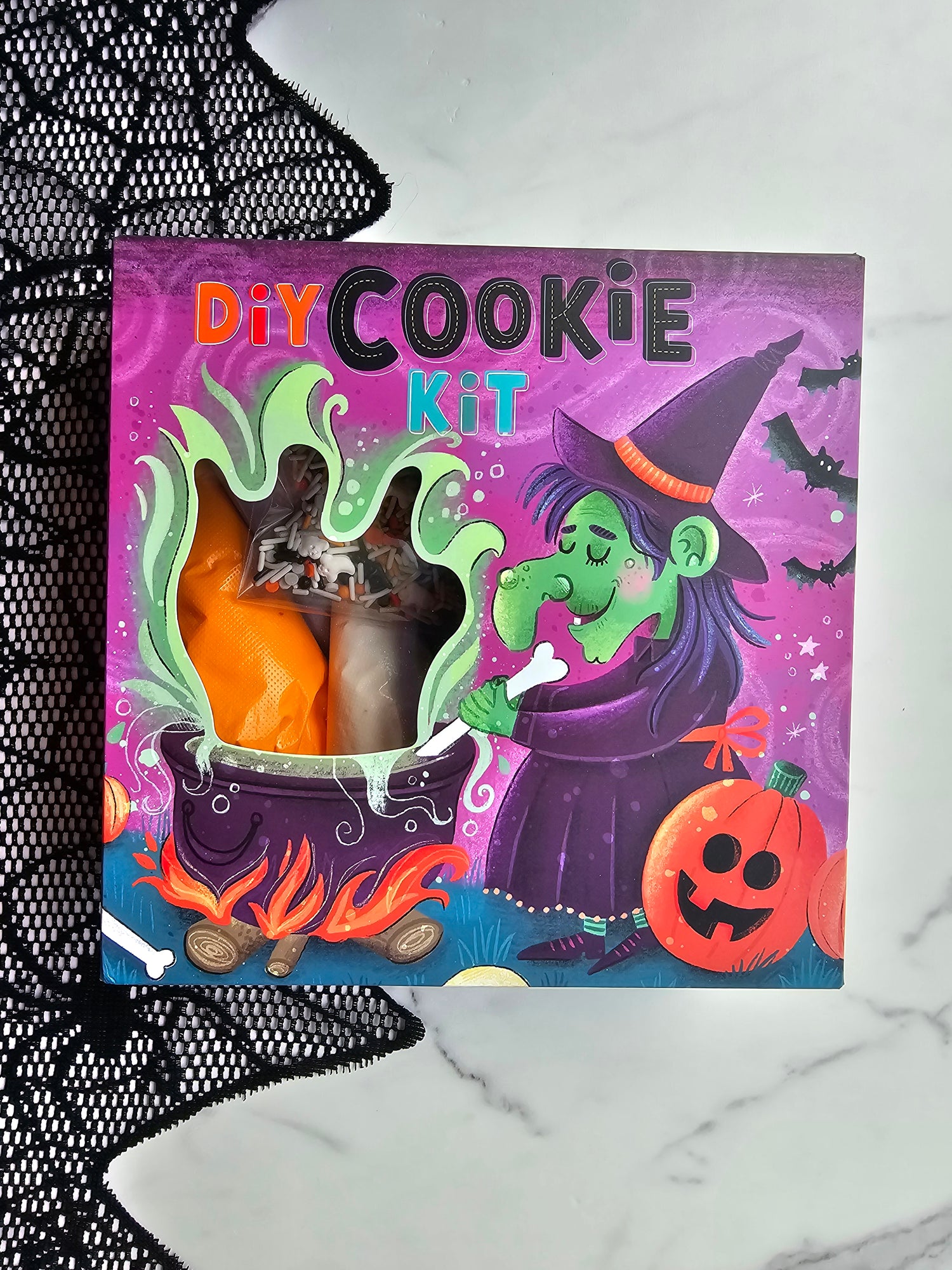Front of purple Halloween DIY Cookie Kit box with witch and cauldron illustration; window shows icing bags and sprinkles inside.