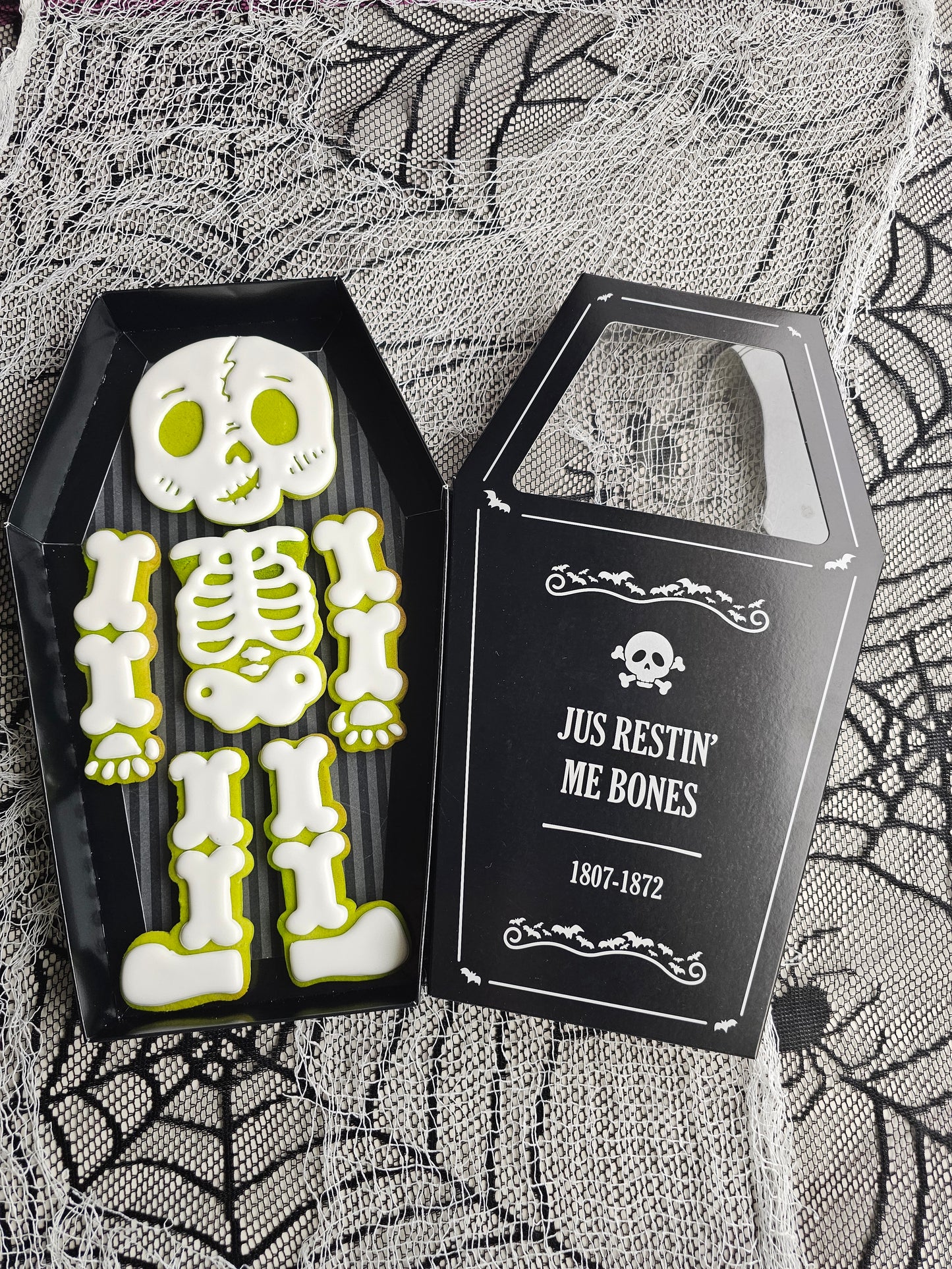Halloween skeleton cookie set with six decorated cookies arranged as a skeleton inside a coffin-shaped black gift box.