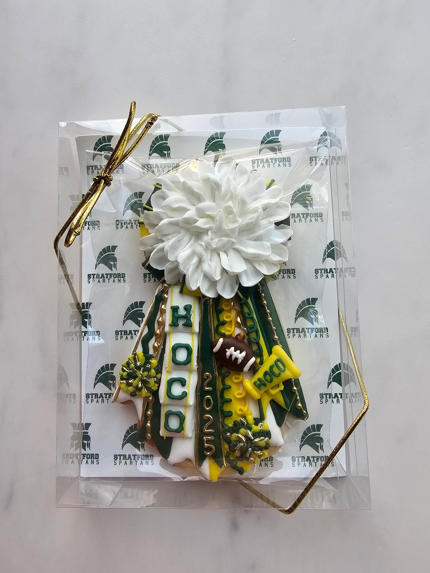 Green, gold, and white homecoming mum cookie with large white chrysanthemum, ‘HOCO’ and ‘2025’ ribbons, football, megaphone, and pom-poms.