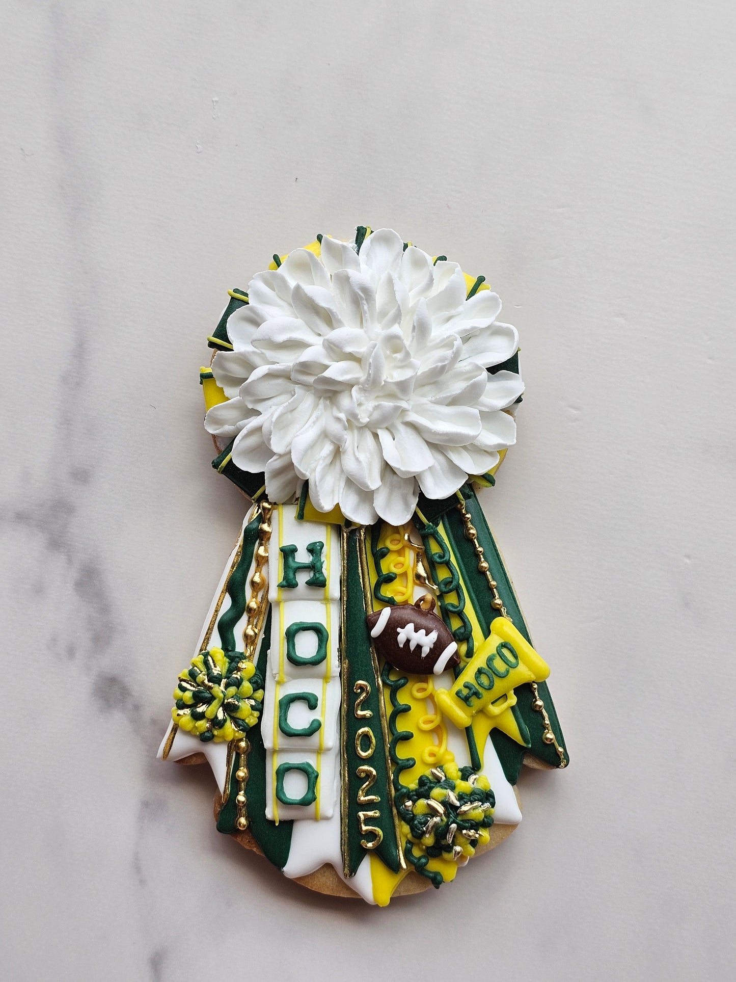 Green, gold, and white homecoming mum cookie with large white chrysanthemum, ‘HOCO’ and ‘2025’ ribbons, football, megaphone, and pom-poms.