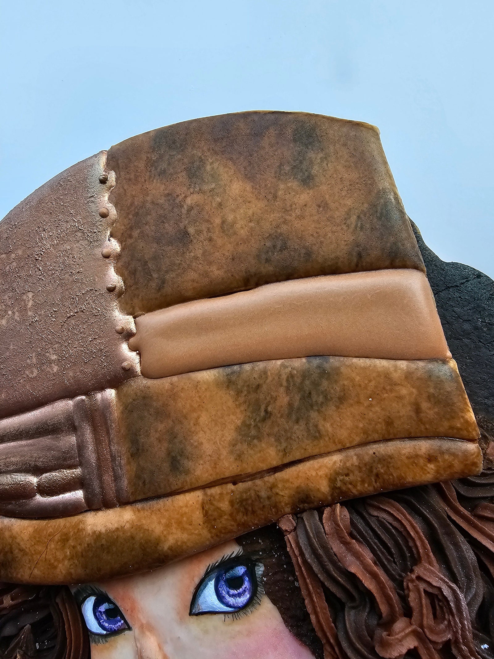 Close-up of a decorated sugar cookie featuring hand-painted royal icing designed to look like realistic brown leather, created using a stippling technique with gel food coloring for textured depth and natural leather grain.
