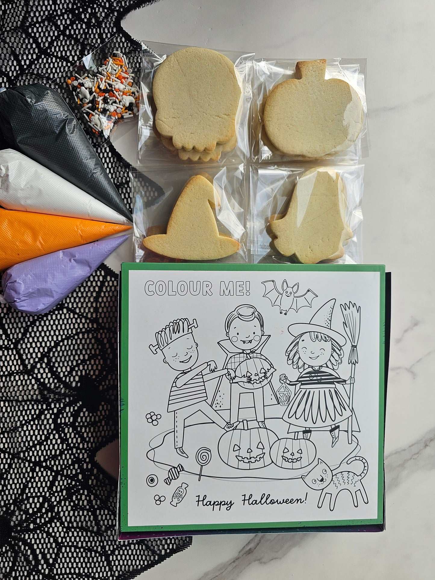 Back of Halloween DIY cookie kit box: skull, pumpkin, witch-hat & ghost cookies, four icing bags, sprinkle mix, and “Colour Me” box back.