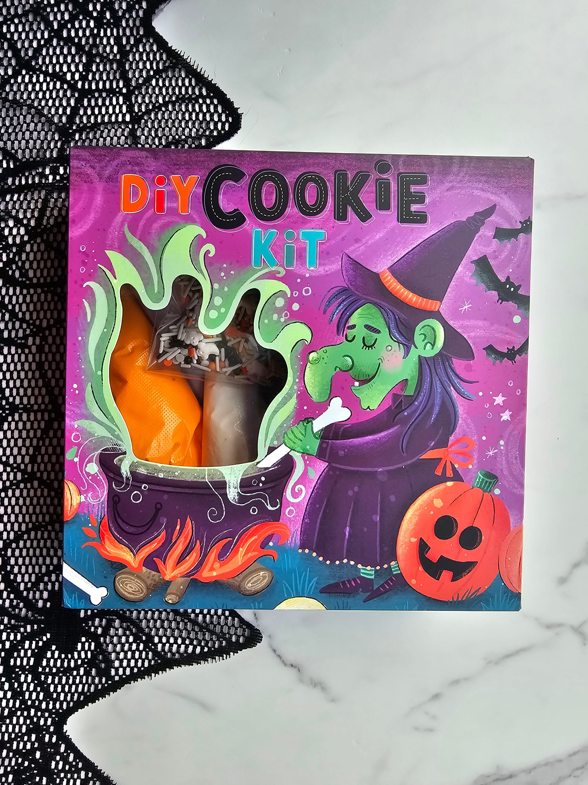 Front of purple Halloween DIY Cookie Kit box with witch and cauldron illustration; window shows icing bags and sprinkles inside.