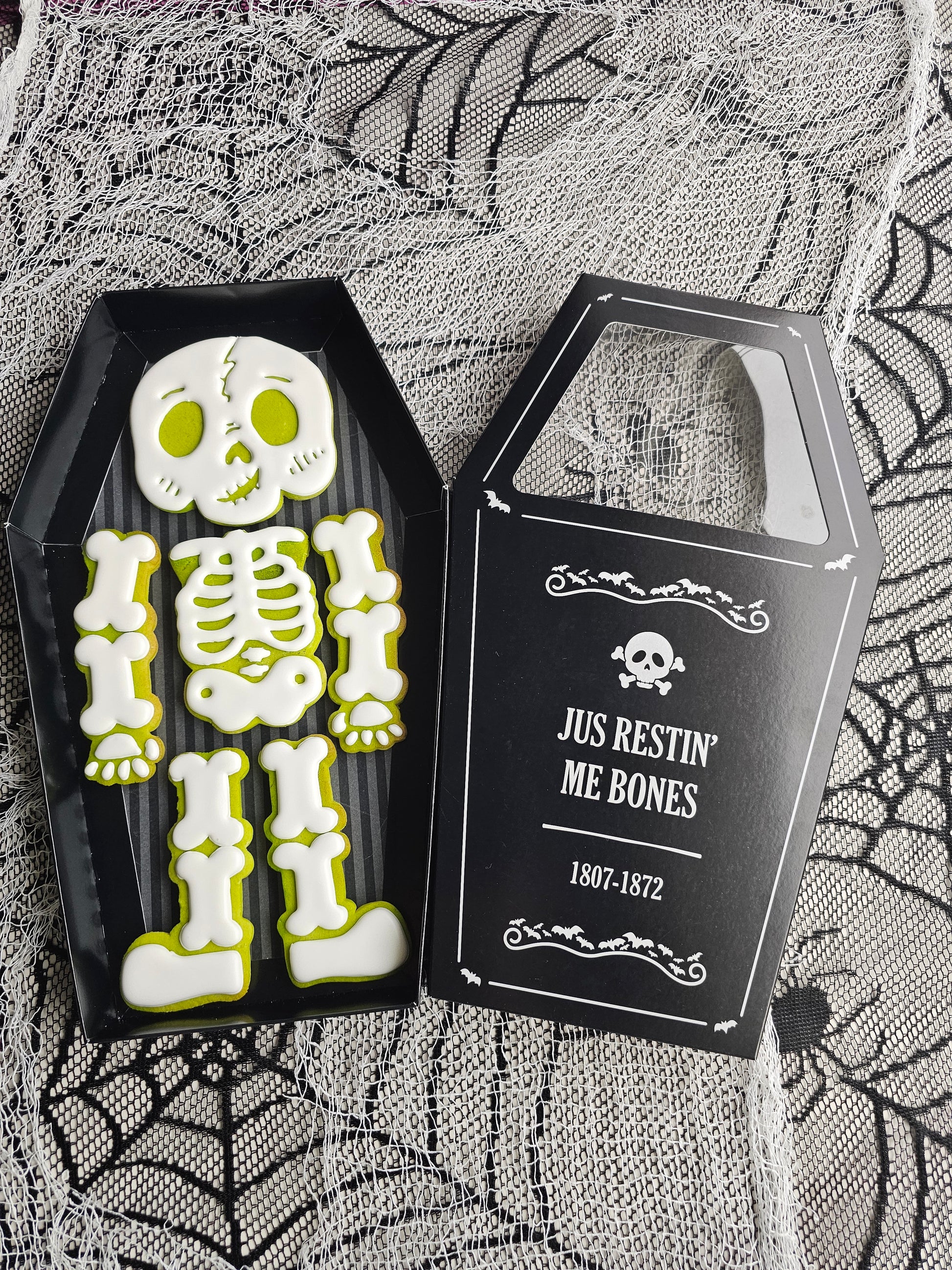 Halloween skeleton cookie set with six decorated cookies arranged as a skeleton inside a coffin-shaped black gift box.