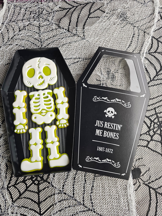 Halloween skeleton cookie set with six decorated cookies arranged as a skeleton inside a coffin-shaped black gift box.