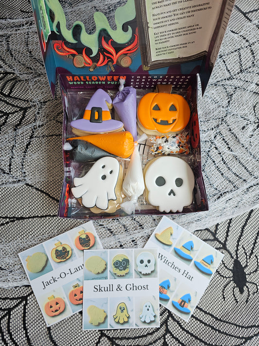 Open Halloween DIY cookie kit in activity box with ghost & witch-hat cookies, four icing bags (orange, black, white, purple) and sprinkles.