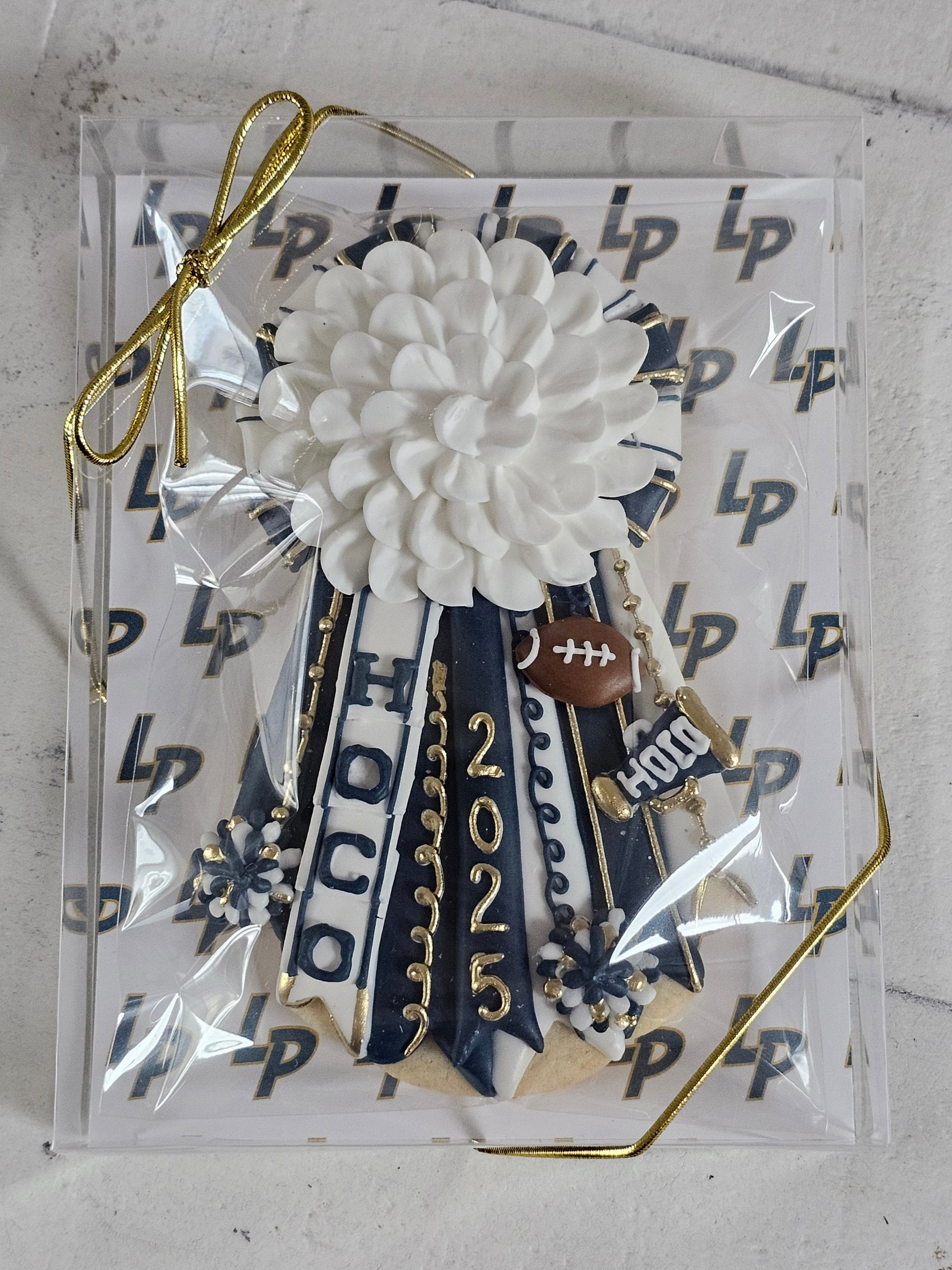 Homecoming mum cookie in white, navy, and gold with Logos Prep School logo background. 